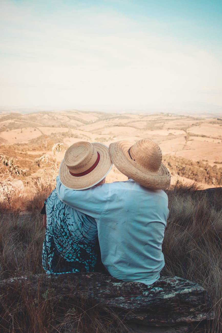 two person wearing sunhats sitting on rock